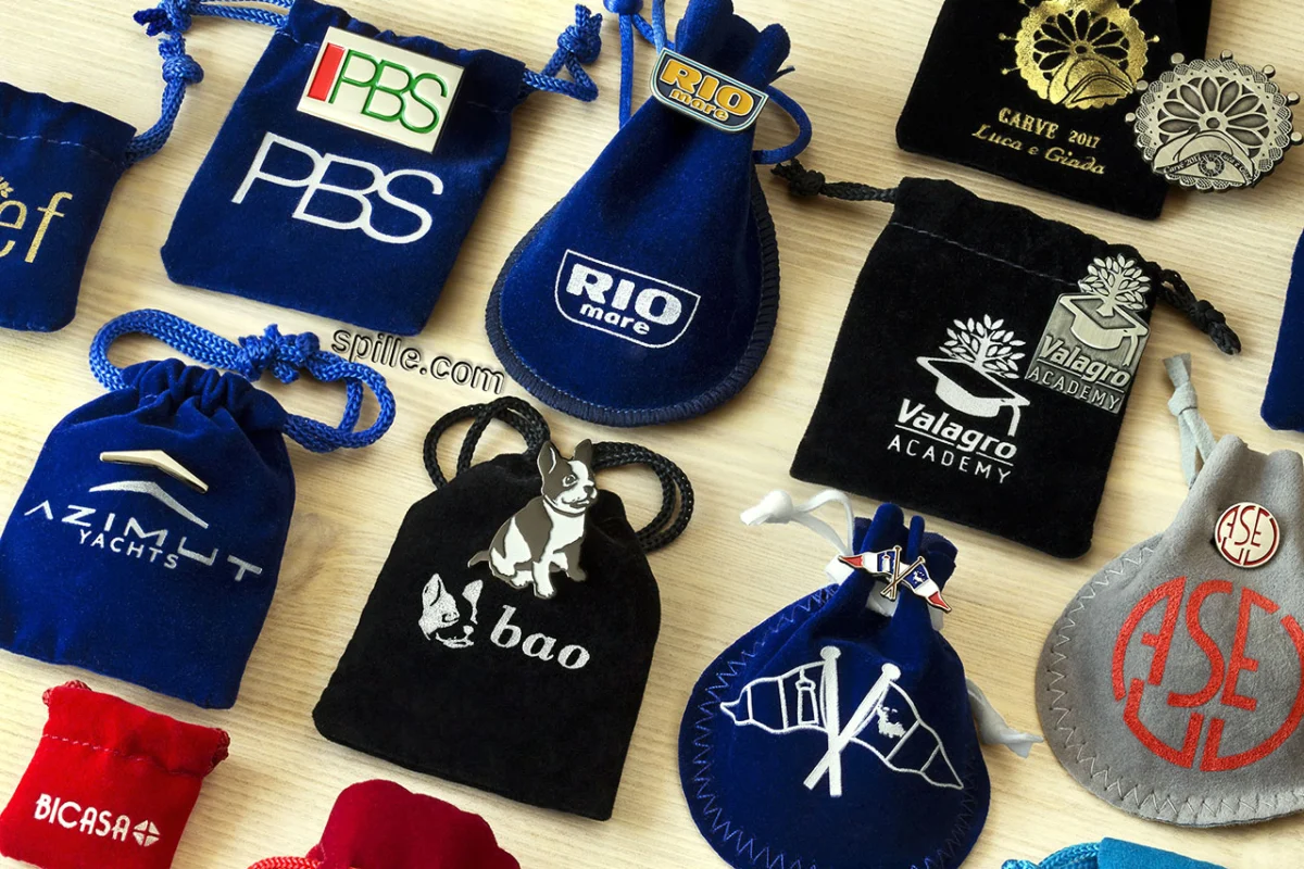 Esempio di spille smaltate classiche con il sacchettino in velluto di vari colori, forme e dimensioni che può essere personalizzato a sua volta con il logo o lo slogan del cliente